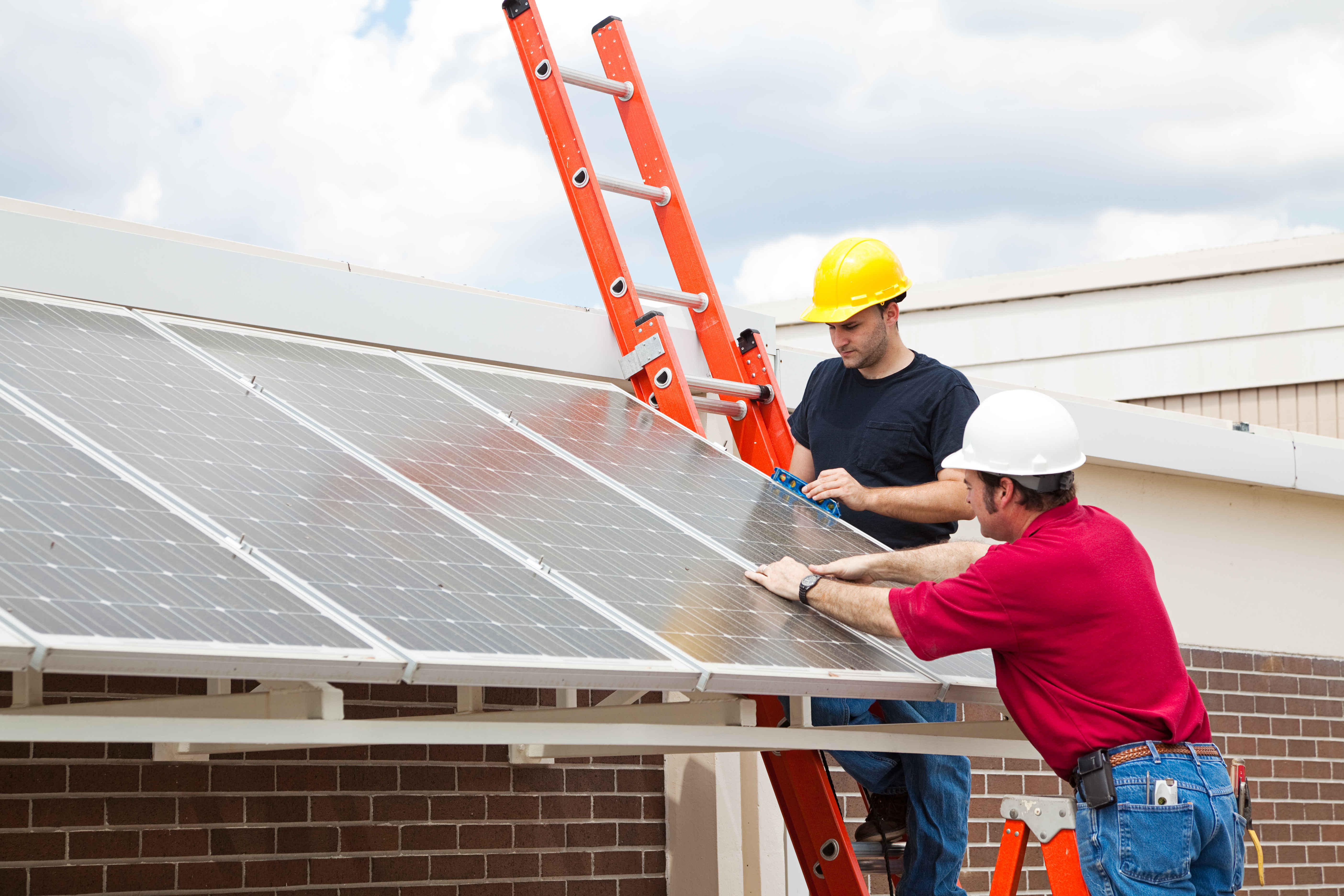 Workers install energy efficient solar panels on the roof of a building.